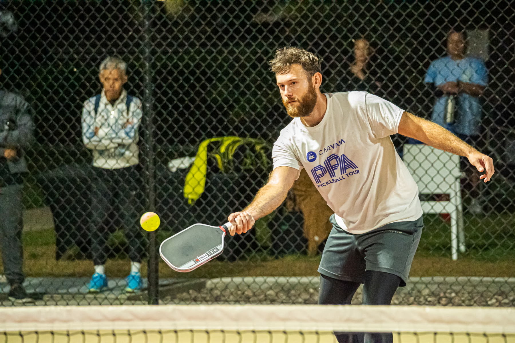 Oliver Lynch reaching for a pickleball at the kitchen line during competitive play